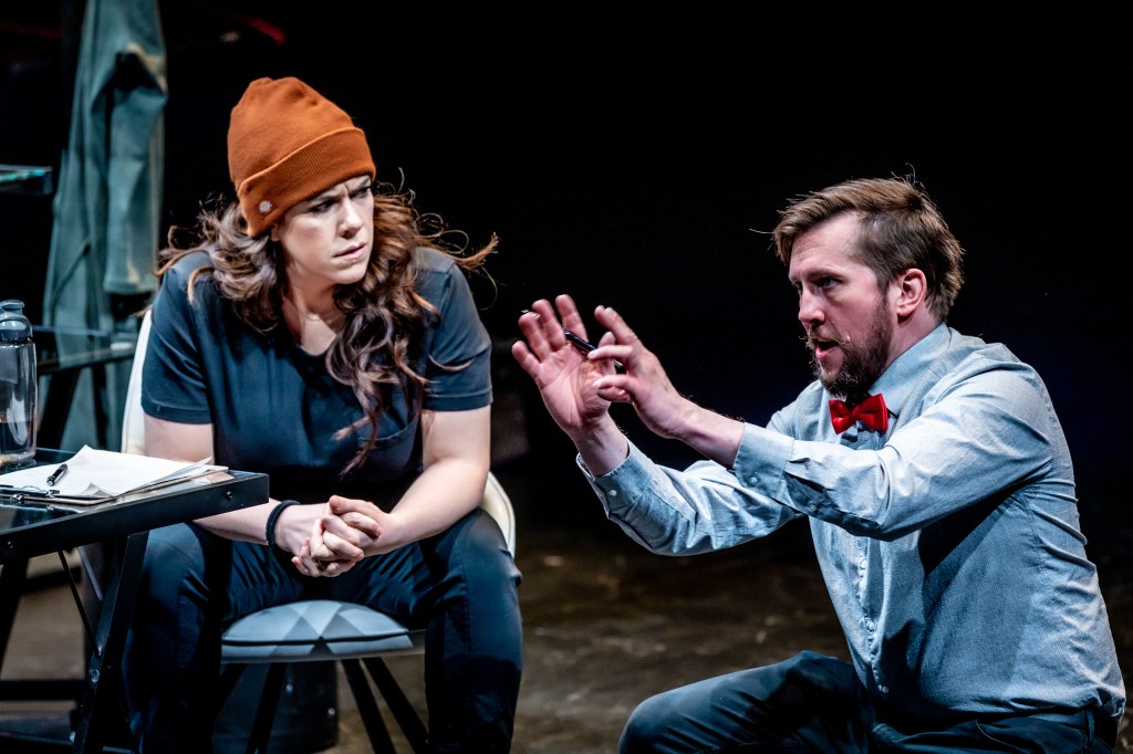 A caucasian, non-binary, female-presenting person seeks counselling from a white, male psychiatrist. The enby person is sitting, looking at the male, who is dominating the conversation and gesticulating.